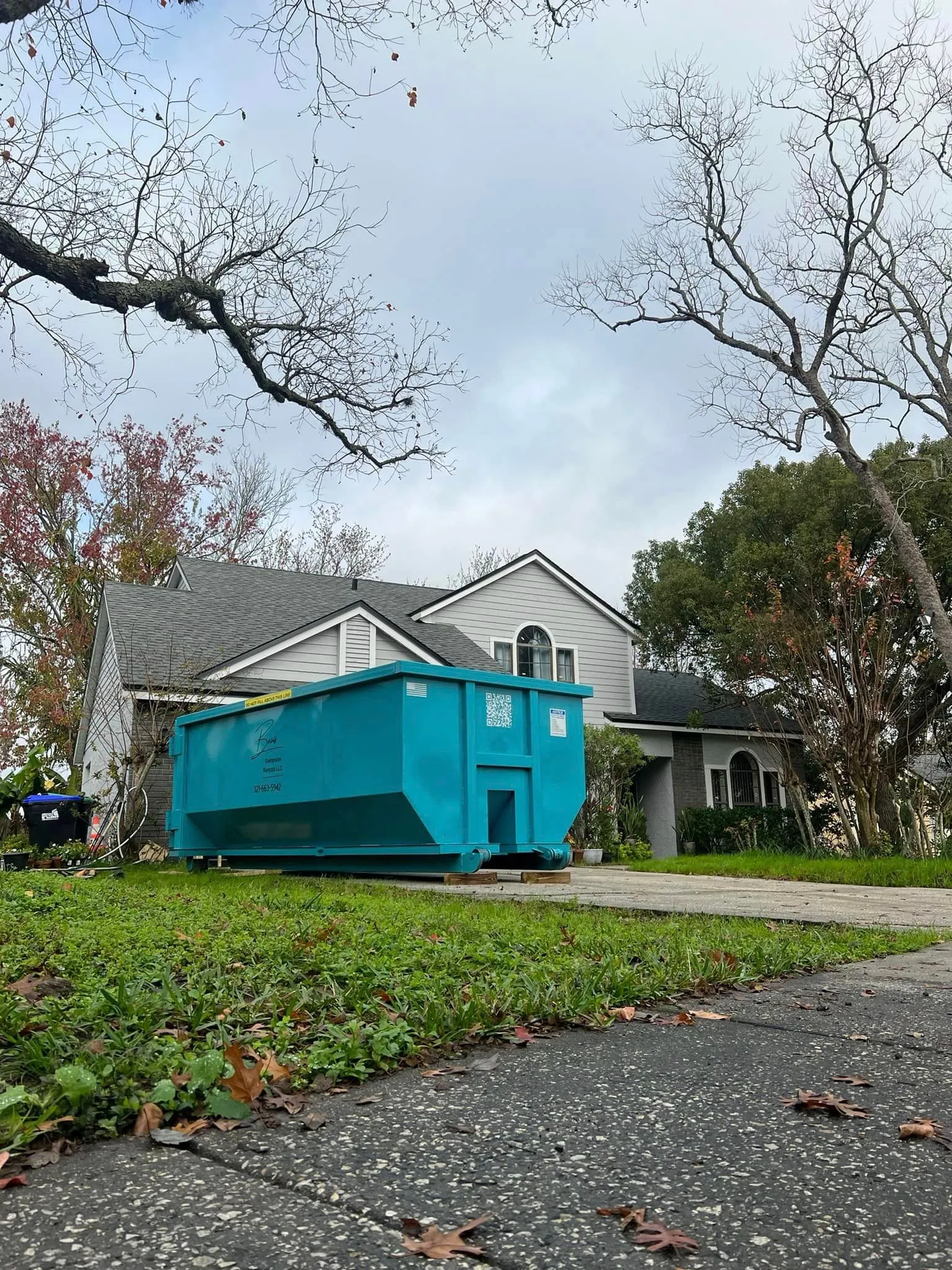 Teal Baus 20 yard roll-off dumpster on a lawn in front of a home in Orlando, FL