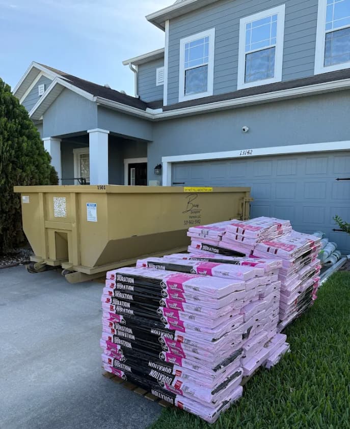 Baus roofing dumpster beside pallets of new shingles at an Orlando, FL home