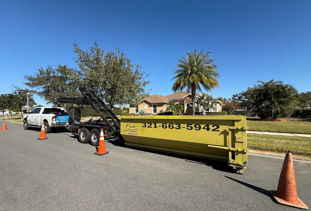 Baus roll-off trailer setting a yellow dumpster at a home in Orlando, FL