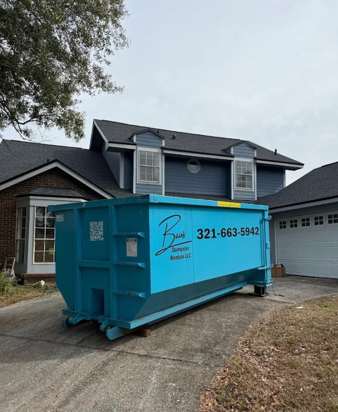 Teal Baus roll-off dumpster parked in a residential driveway