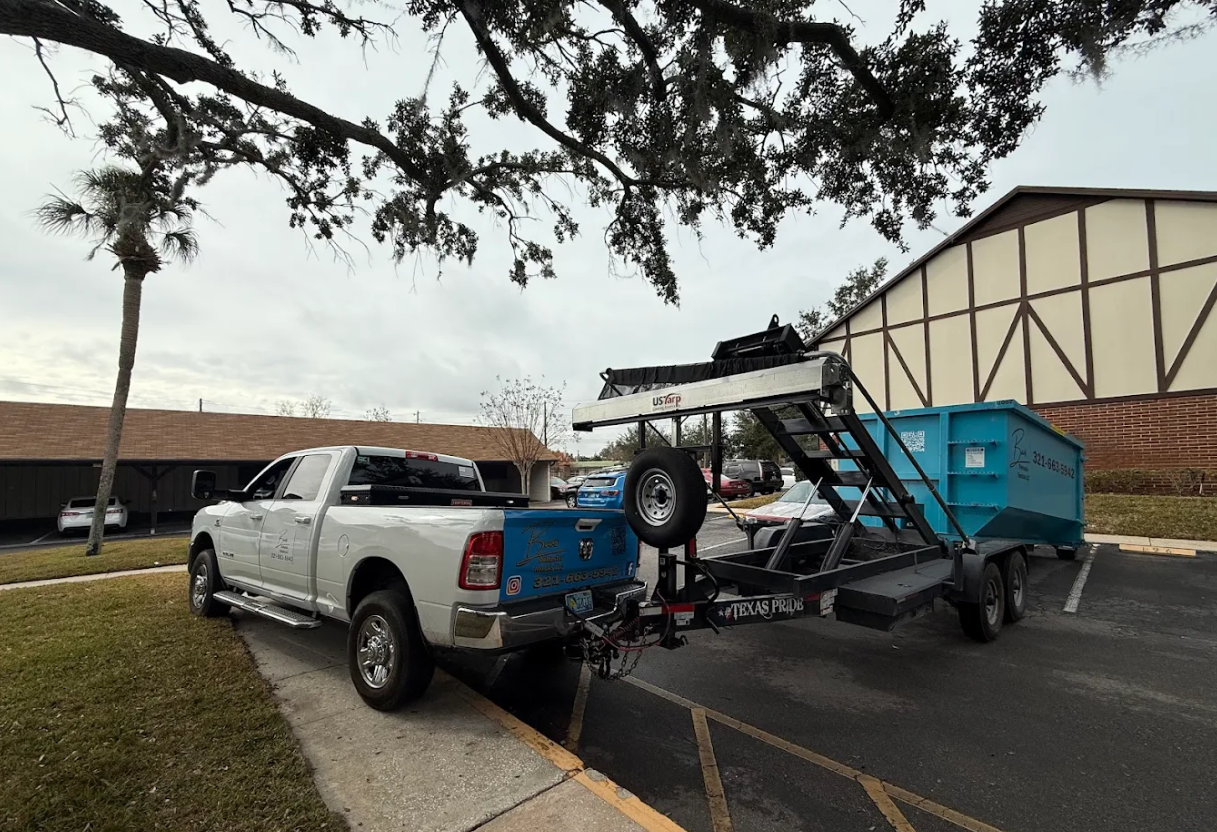 Baus Dumpster Rentals truck towing a blue roll-off dumpster on a trailer in Orlando, FL