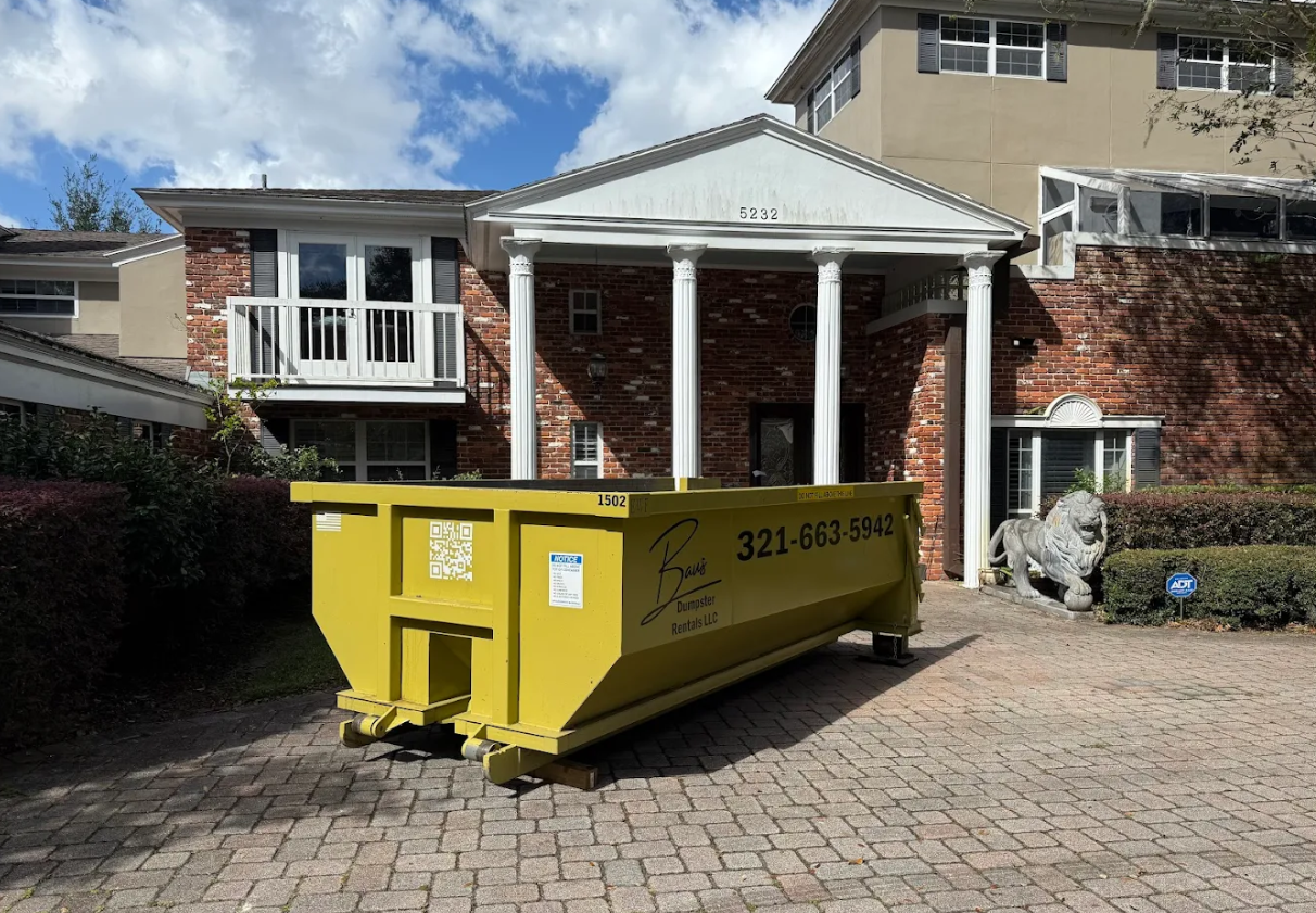 Yellow Baus roll-off dumpster on a brick driveway in Lake Nona, FL